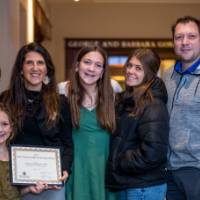 A faculty member's family smiles with them and their award